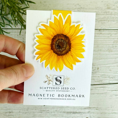 Magnetic bookmark with sunflower design held by a hand on a wooden surface - The Book Keeper and Co