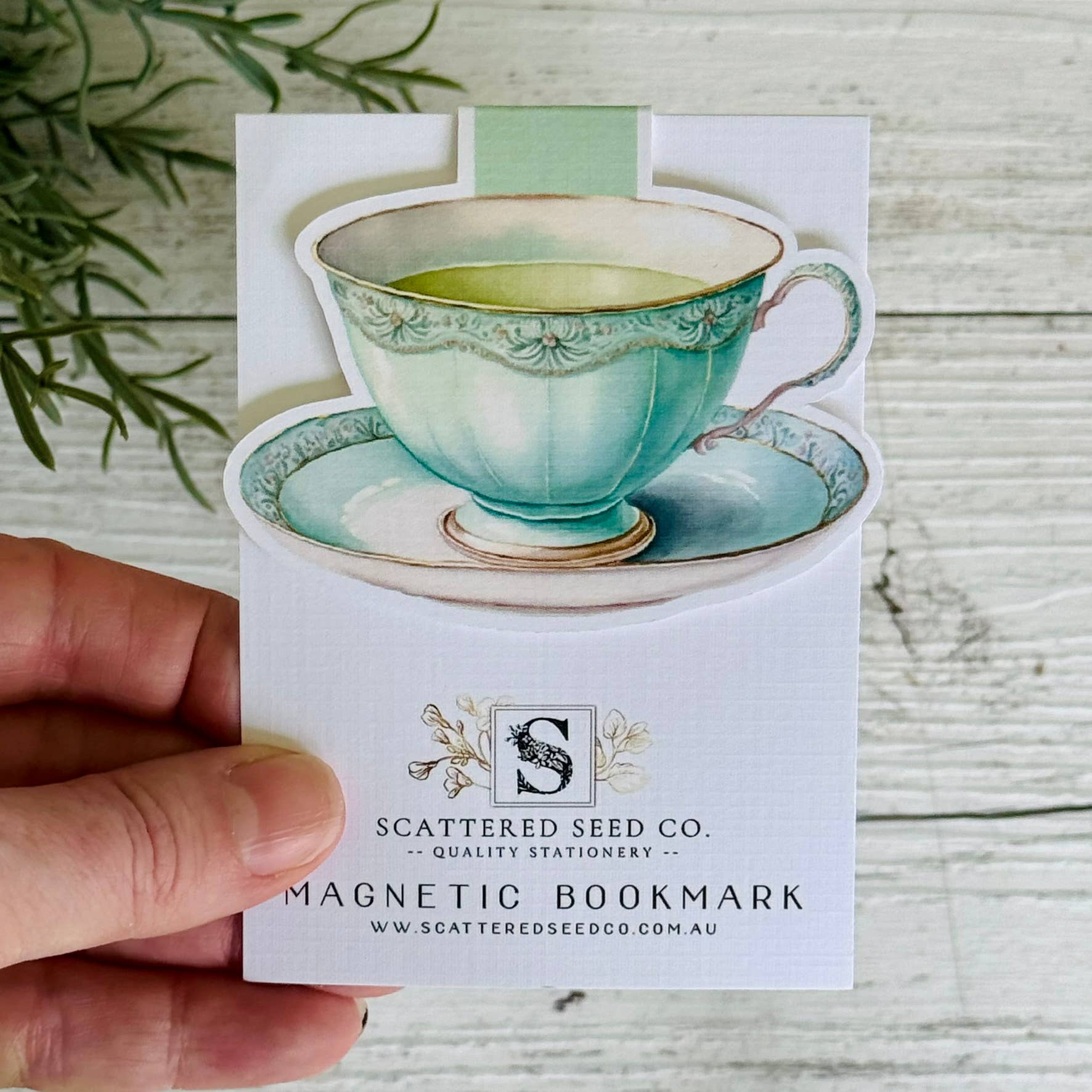 Magnetic bookmark with a teacup design held by a hand on a wooden surface - The Book Keeper & Co