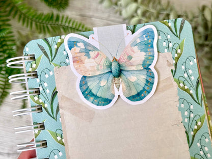 Notebook with a decorative butterfly bookmark  on a green leafy background. - the book keeper and Co