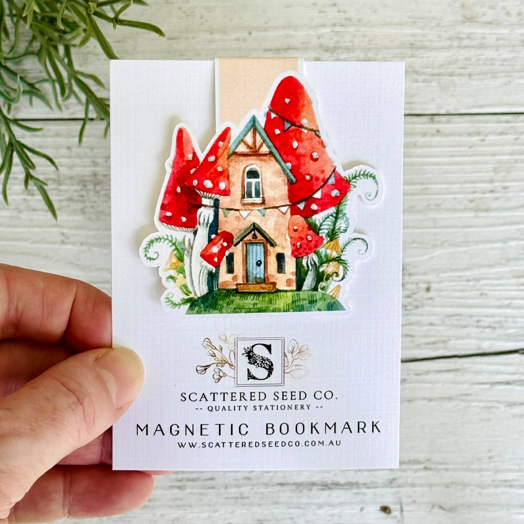 Magnetic bookmark with mushroom house design held by a hand on a wooden surface - The Book Keeper and Co