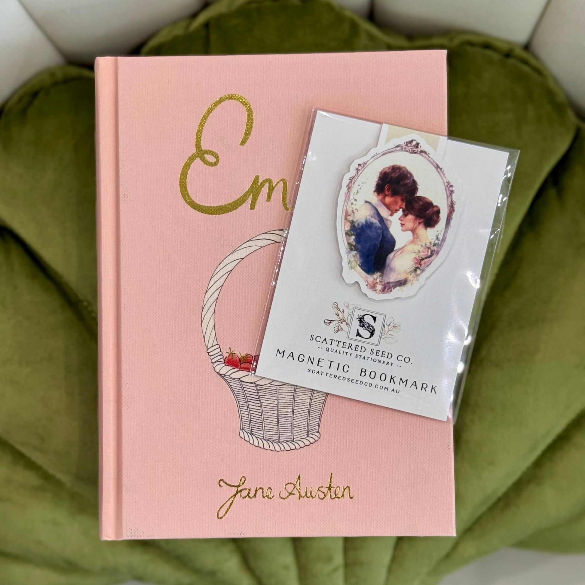 Pink book with 'Em' and 'Jane Austen' text, featuring a magnetic bookmark on a green  fabric background- The Book Keeper and Co