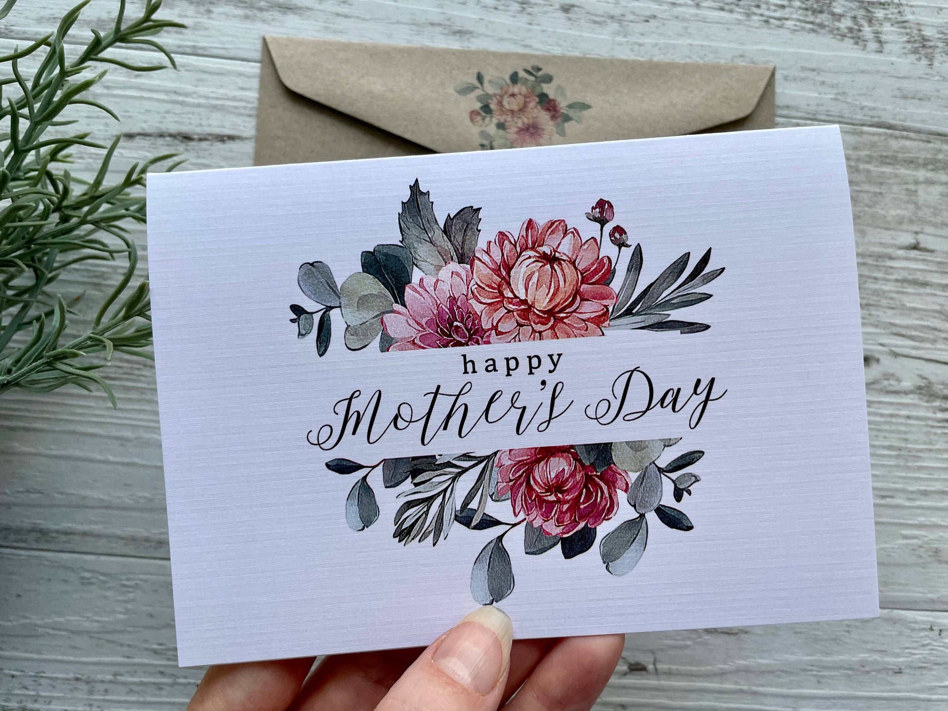 Mother's Day card with floral design held by a hand on a wooden surface.