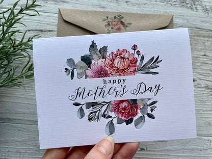 Mother's Day card with floral design held by a hand on a wooden surface.