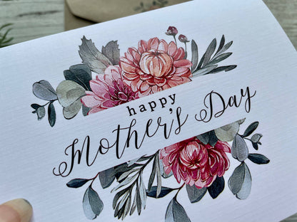Greeting card with floral design and 'Happy Mother's Day' text on a wooden surface.