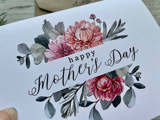 Greeting card with floral design and 'Happy Mother's Day' text on a wooden surface.