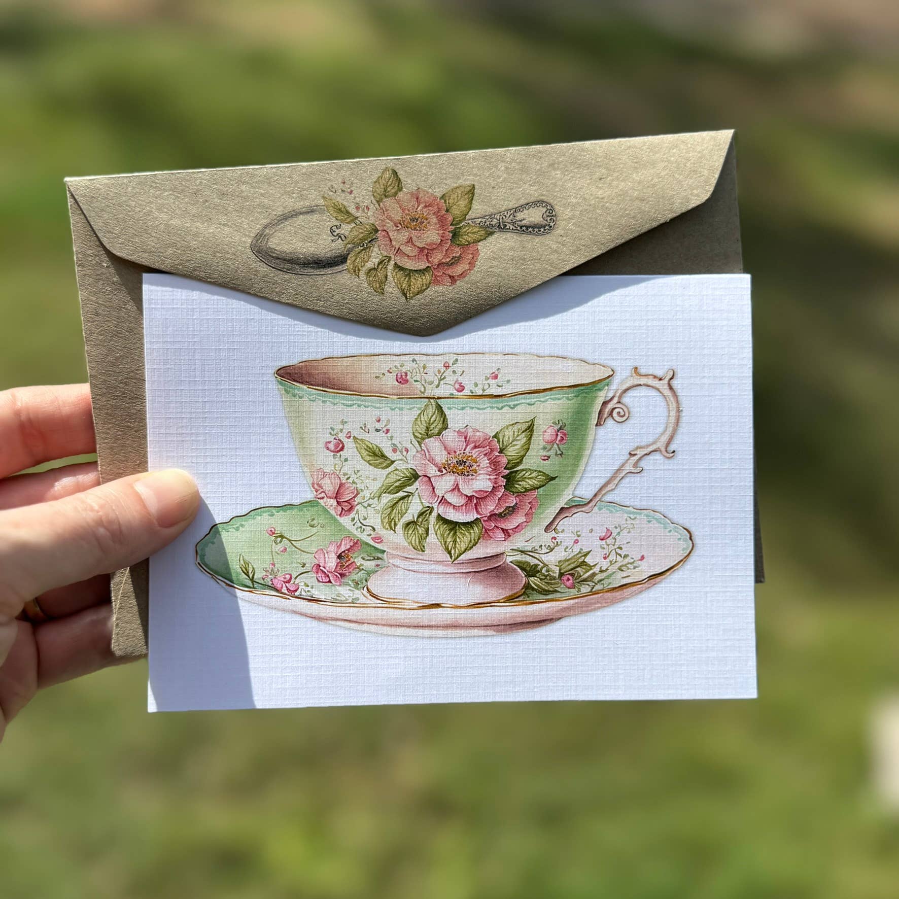 Card with floral teacup design held by a hand against a blurred natural background - the Book Keeper & Co