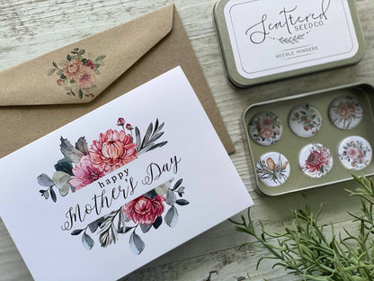 Mother's Day card with floral design, envelope, and decorative tins on a wooden surface.
