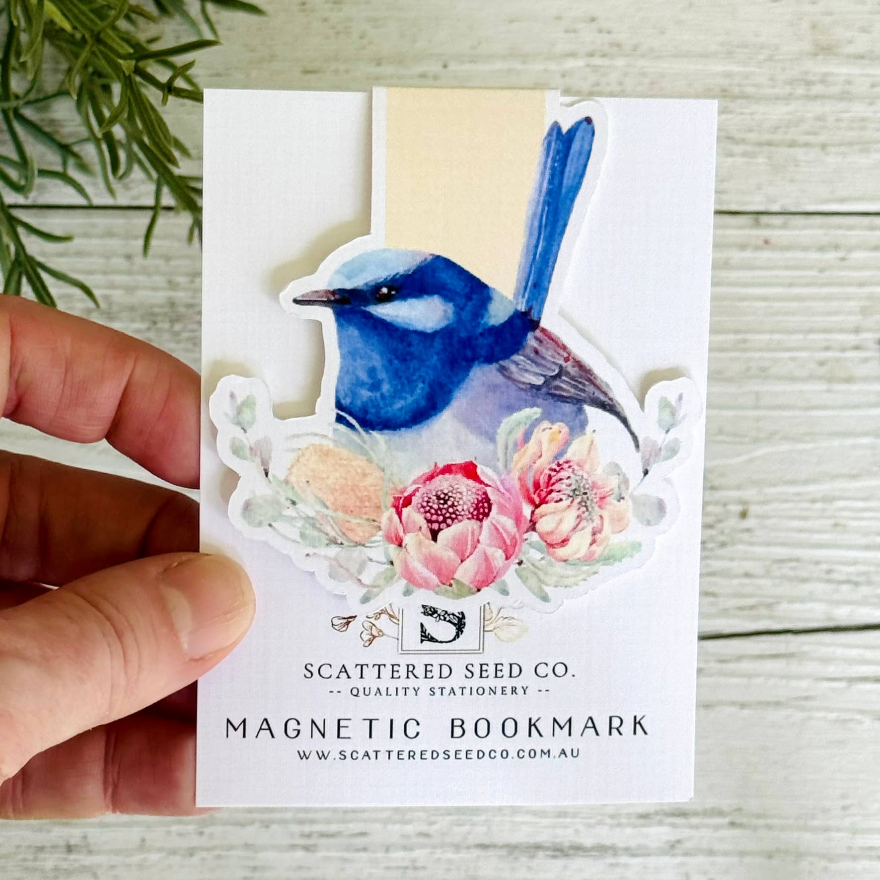 Magnetic bookmark with a blue bird design held by a hand on a wooden surface - The Book Keeper and Co
