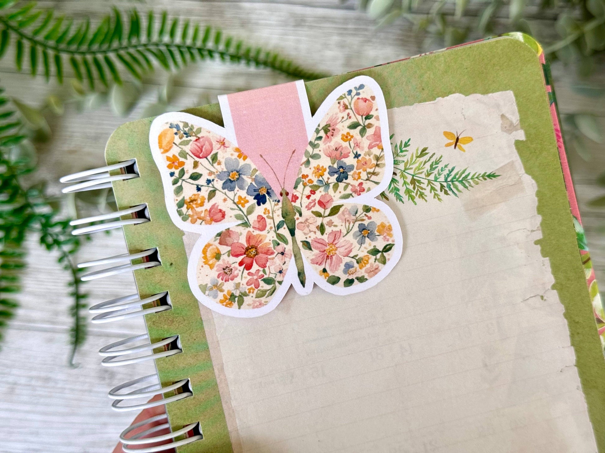 Butterfly-shaped floral bookmark on a notebook with green leaves in the background - The Book Keeper and Co