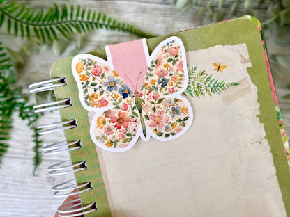 Butterfly-shaped floral bookmark on a notebook with green leaves in the background - The Book Keeper and Co